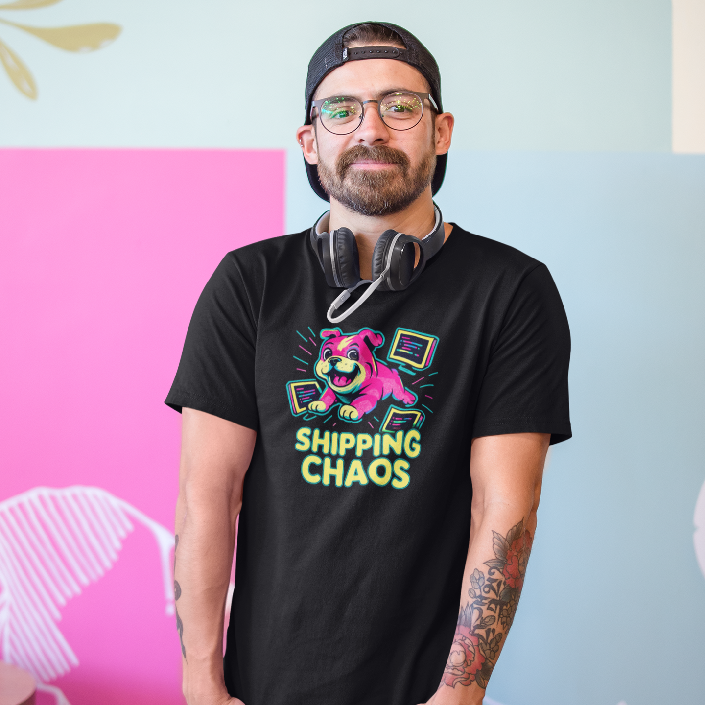 Man wearing a black t-shirt with colorful graphics and text, standing against a multicolored wall.