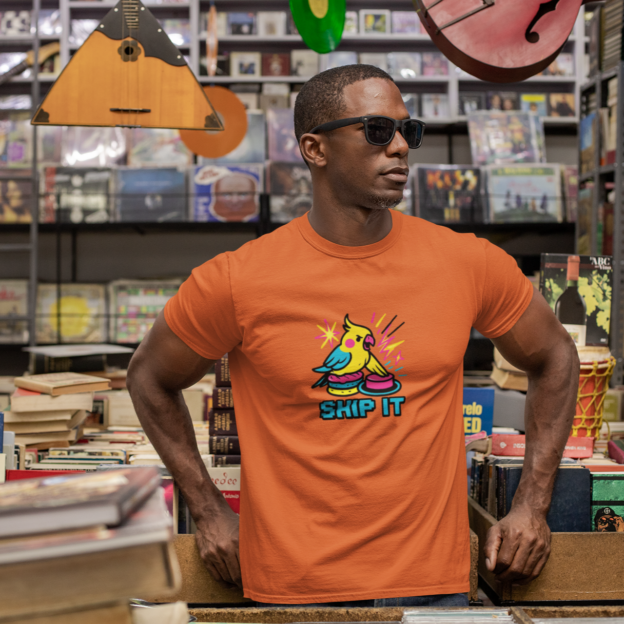 Man wearing an orange t-shirt with a colorful graphic design in a music store.