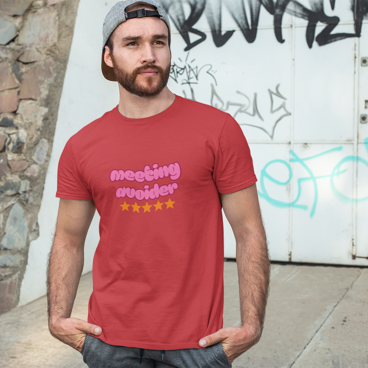 Man wearing a red t-shirt with text standing against a graffiti-covered wall.