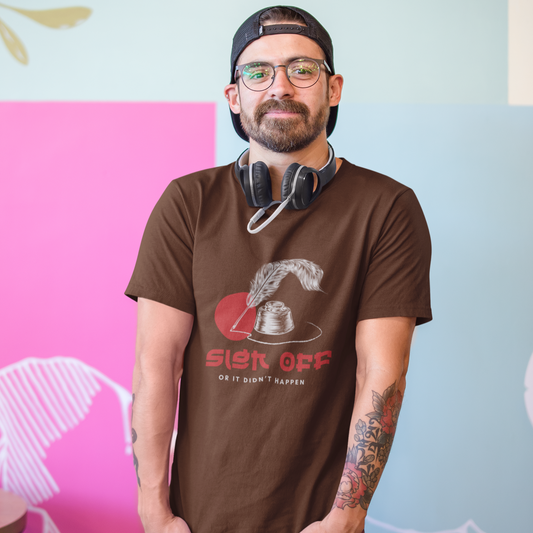 Man wearing a brown t-shirt with text and graphics, standing against a colorful wall.