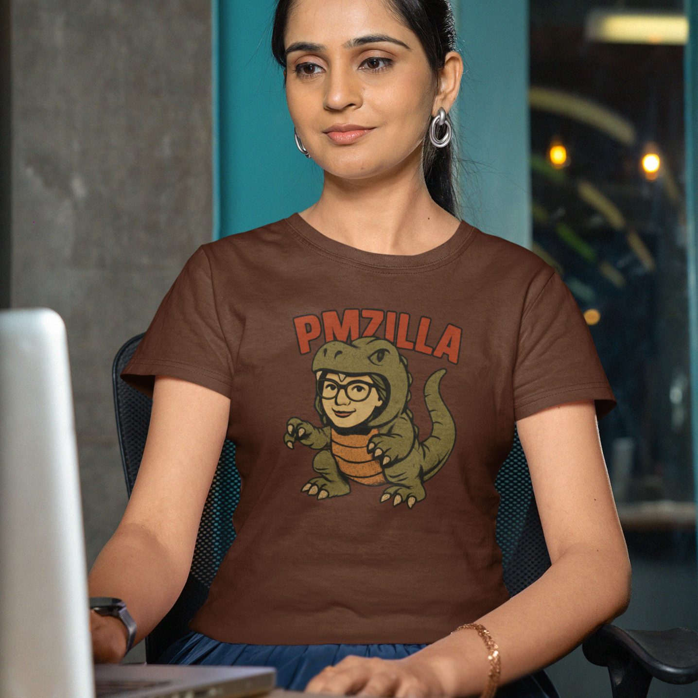 Woman wearing a brown t-shirt with a graphic design sitting at a desk.