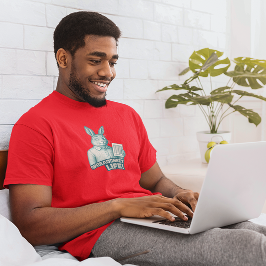 Man in a red shirt using a laptop on a bed with a plant in the background