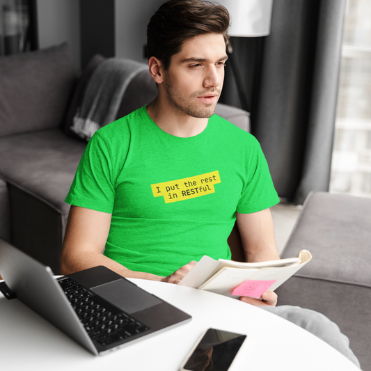 Man in a green t-shirt sitting at a table with a laptop and a book, in a living room setting.