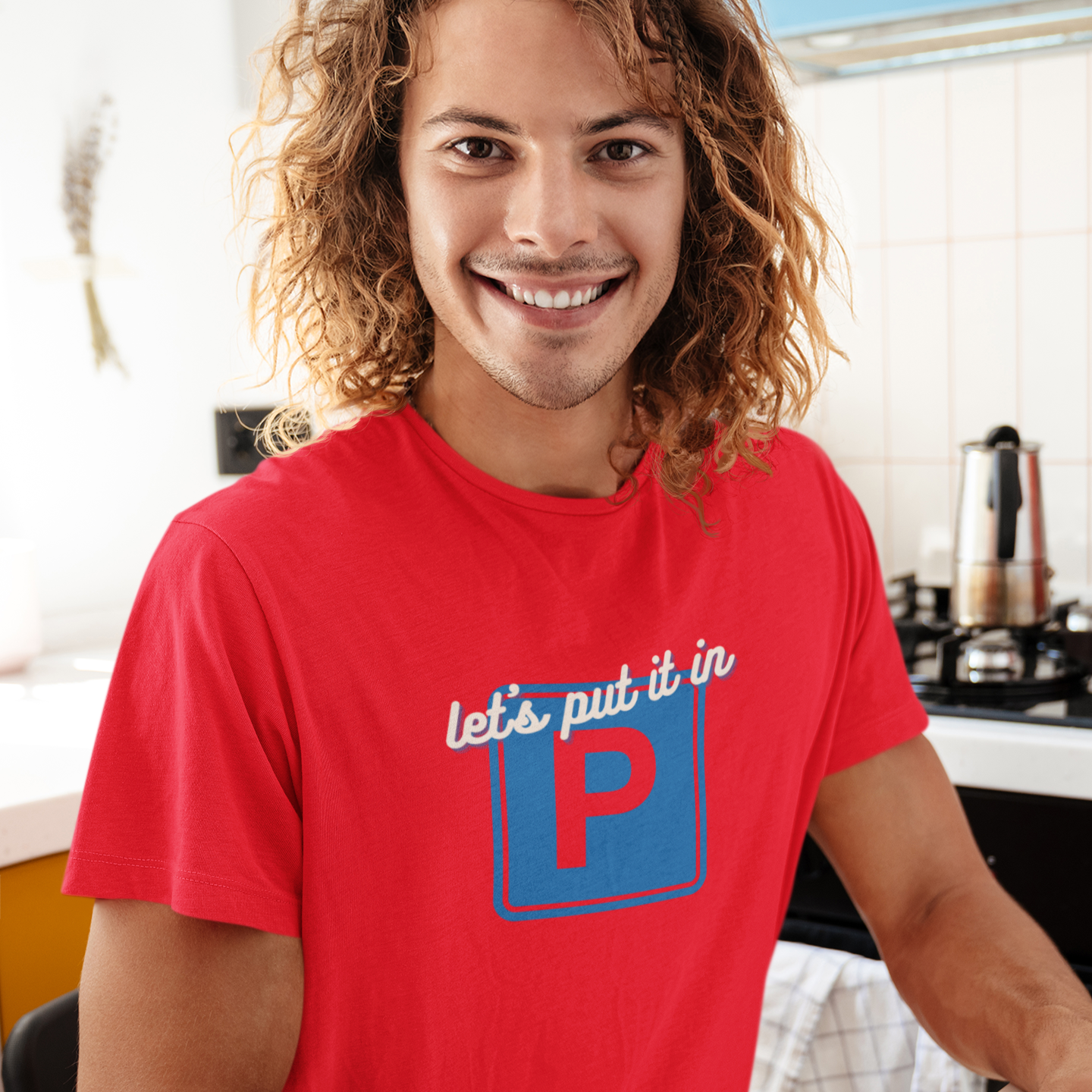 Man wearing a red t-shirt with a logo and text, sitting at a desk.