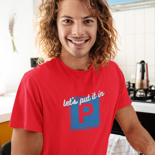 Man wearing a red t-shirt with a logo and text, sitting at a desk.