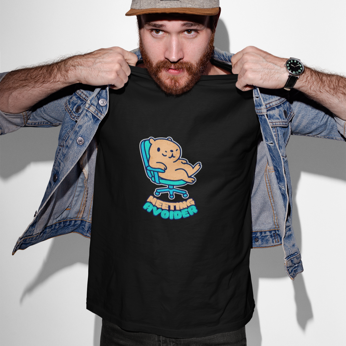 Man wearing a black t-shirt with a graphic design, denim jacket, and cap on a white background