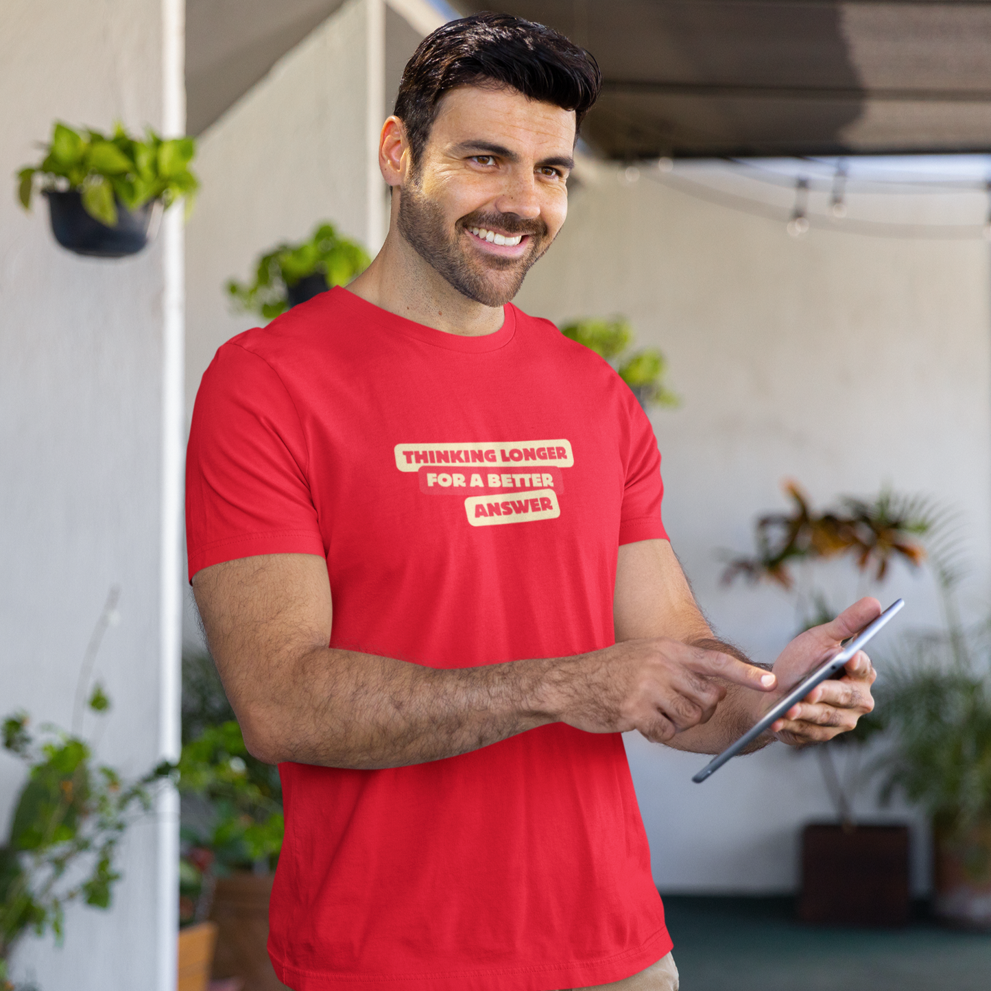 Man wearing a red t-shirt with text, holding a tablet outdoors.