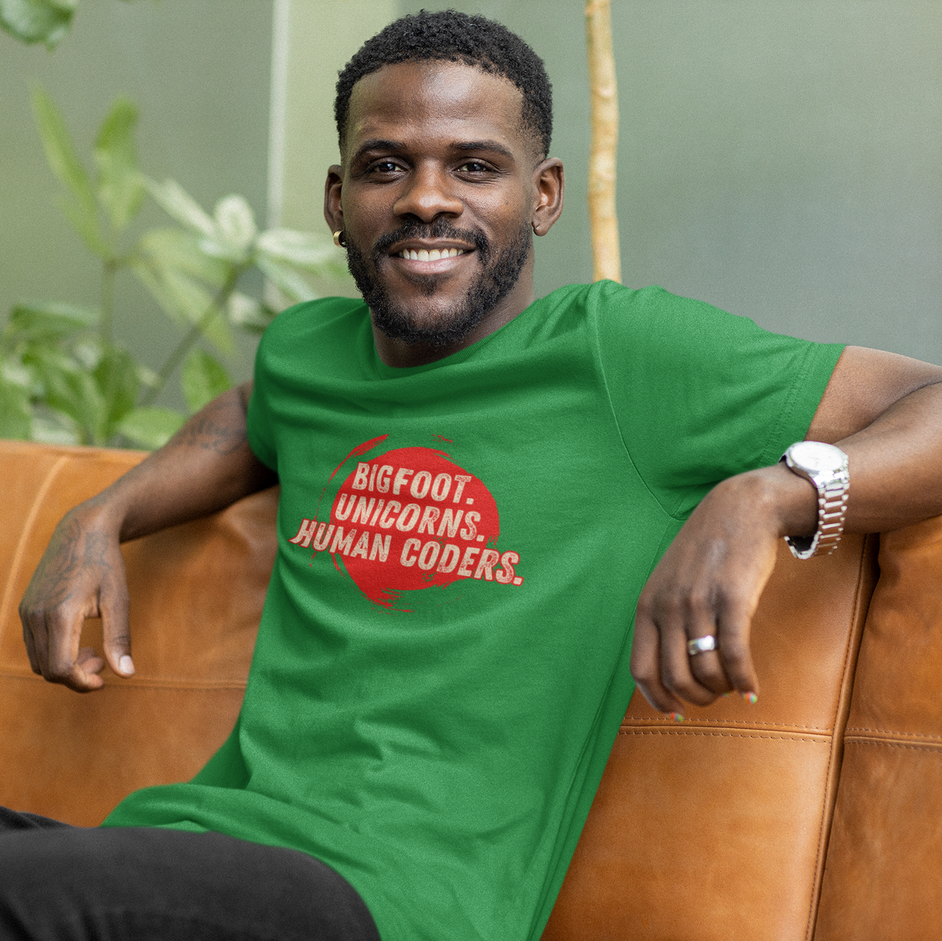 Man wearing a green t-shirt with text sitting on a brown couch outdoors.