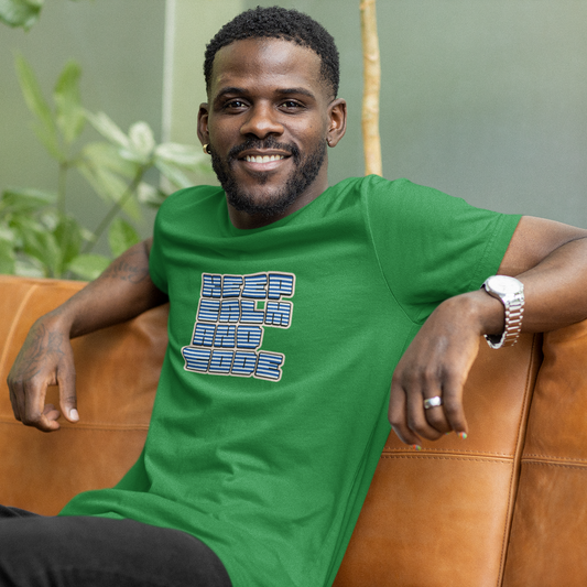 Man wearing a green t-shirt with a graphic design, sitting on a brown couch with a blurred green plant background.