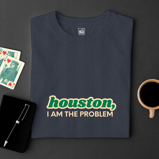 Navy blue t-shirt with 'Houston, I am the problem' text on a dark surface with cards and a cup.