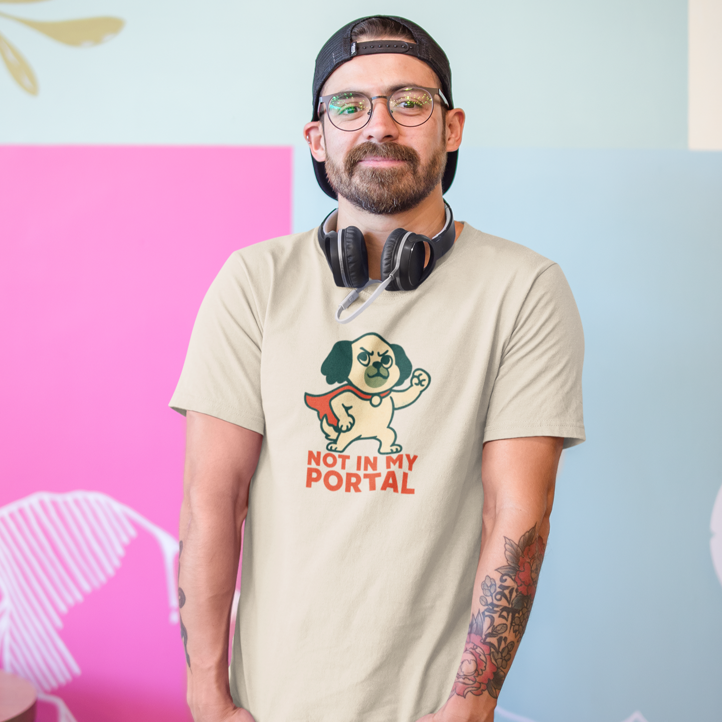 Man wearing a beige t-shirt with a graphic design and text, standing against a colorful wall.