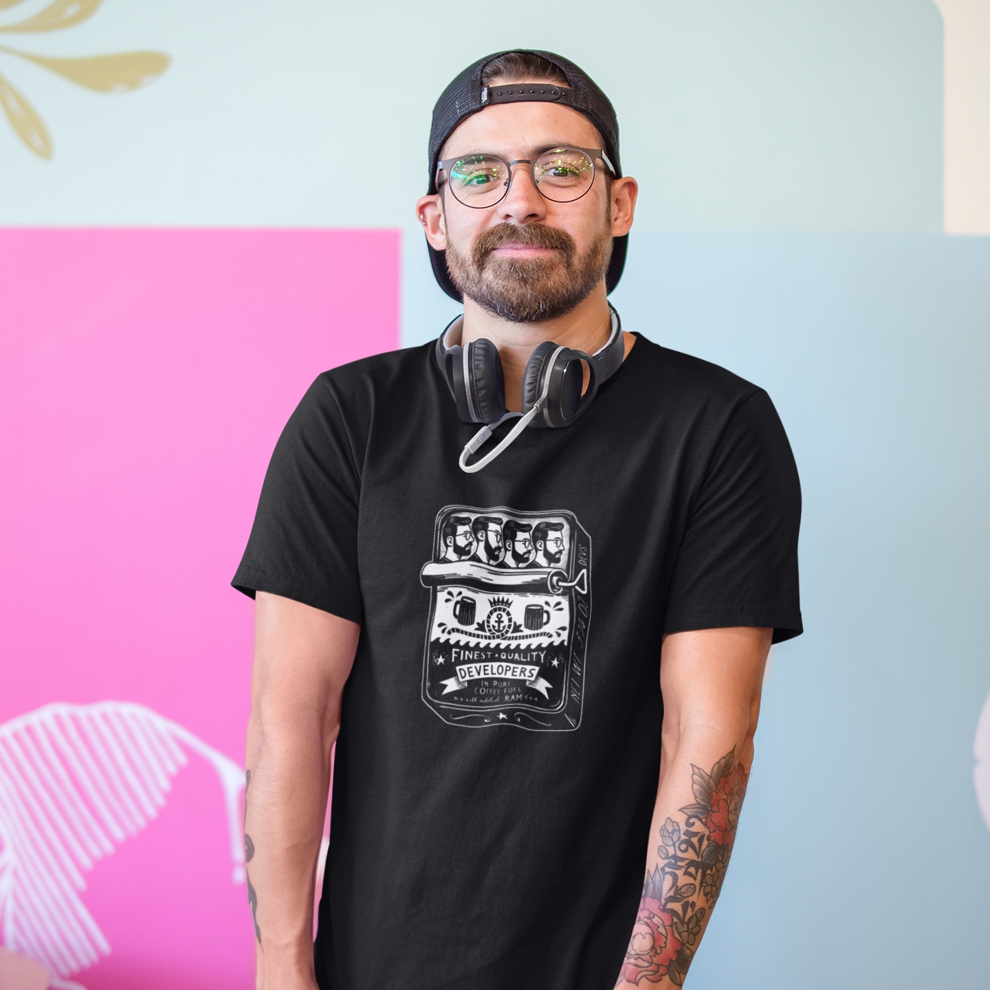 Man wearing a black t-shirt with a graphic design, red pants, and a cap, standing against a colorful wall.