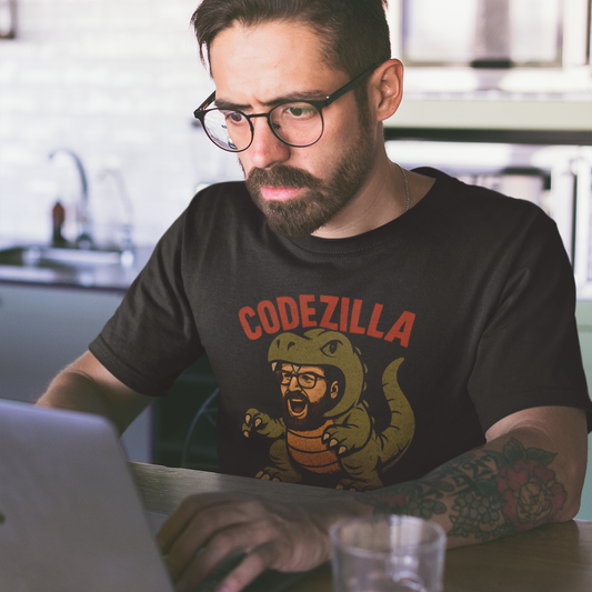 Man wearing a 'Codezilla' t-shirt using a laptop in a kitchen.