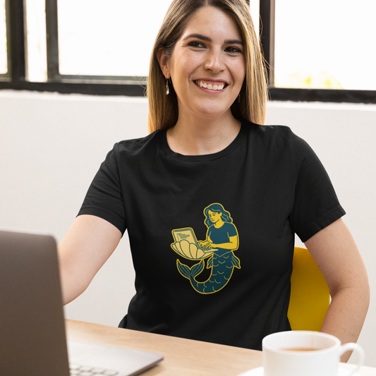 Woman wearing a black t-shirt with a graphic design, sitting at a desk with a laptop and coffee.
