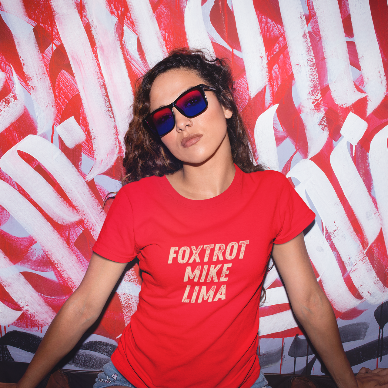 Person wearing a red 'FOXTROT MIKE LIMA' t-shirt in front of a colorful abstract background