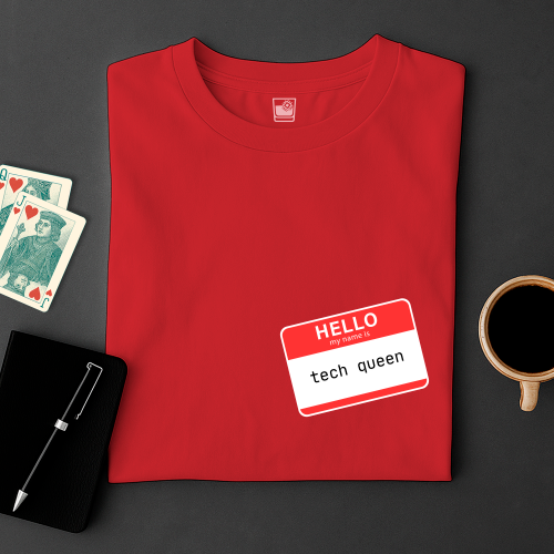 Red t-shirt with a name tag saying 'HELLO tech queen' on a dark surface with playing cards and a coffee cup.