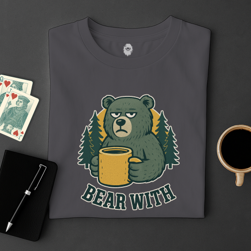 Gray t-shirt with a bear holding a mug graphic and 'Bear With' text, placed on a dark surface with cards and a coffee cup.