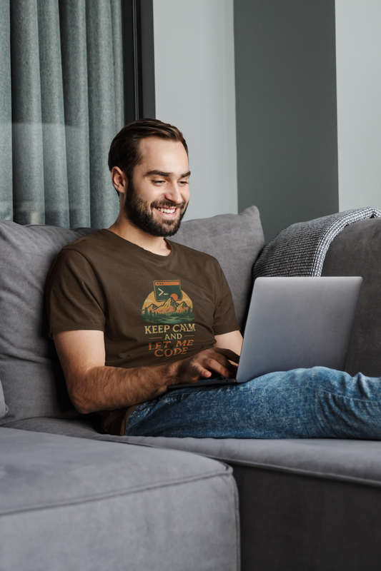 Man sitting on a couch using a laptop, wearing a brown t-shirt with a graphic design.