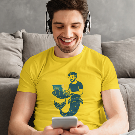 Man wearing a yellow t-shirt with a mermaid graphic, sitting on a couch and using a phone.