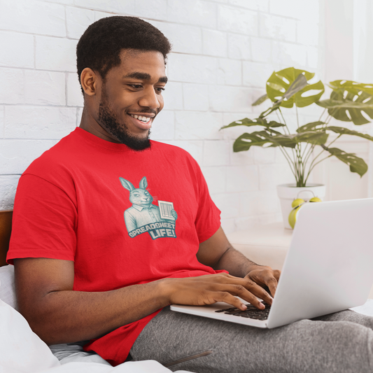 Man in a red shirt using a laptop on a bed with a plant in the background