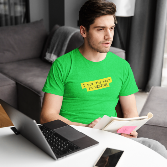 Man in a green t-shirt sitting at a table with a laptop and a book, wearing a yellow badge that read : I put the rest in RESTful