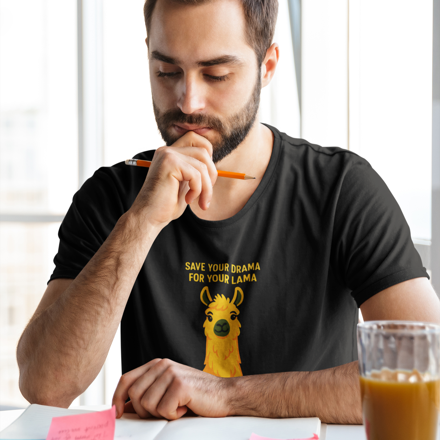 Man wearing a black t-shirt with a llama graphic and text, sitting at a table with a glass of coffee.