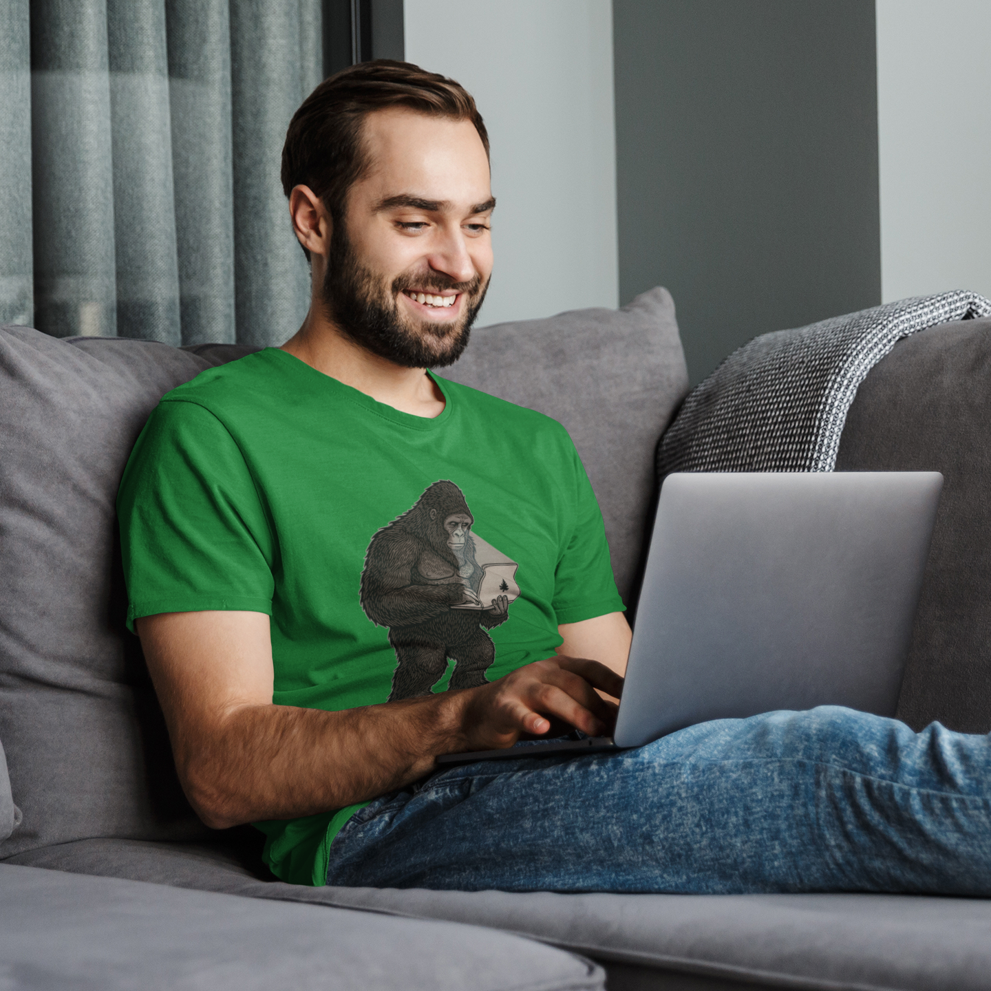 Man in a green t-shirt using a laptop on a gray couch.