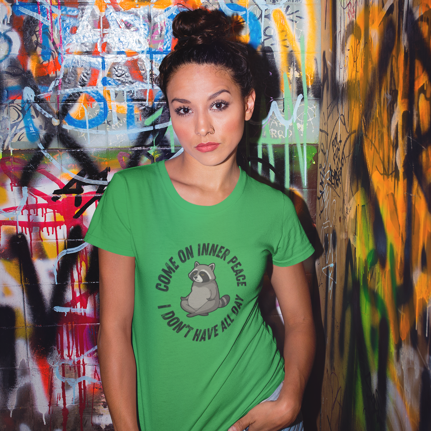 Woman wearing a green t-shirt with text and graphics in front of a graffiti-covered wall.